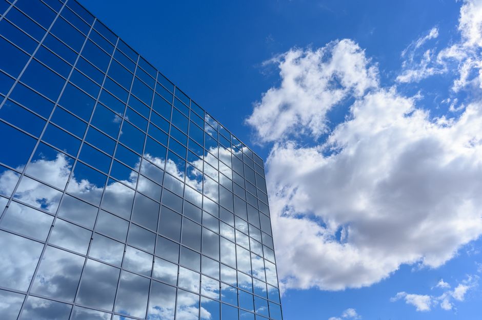 Contemporary skyscraper with glass facade reflecting clouds and blue sky, urban architectural design.